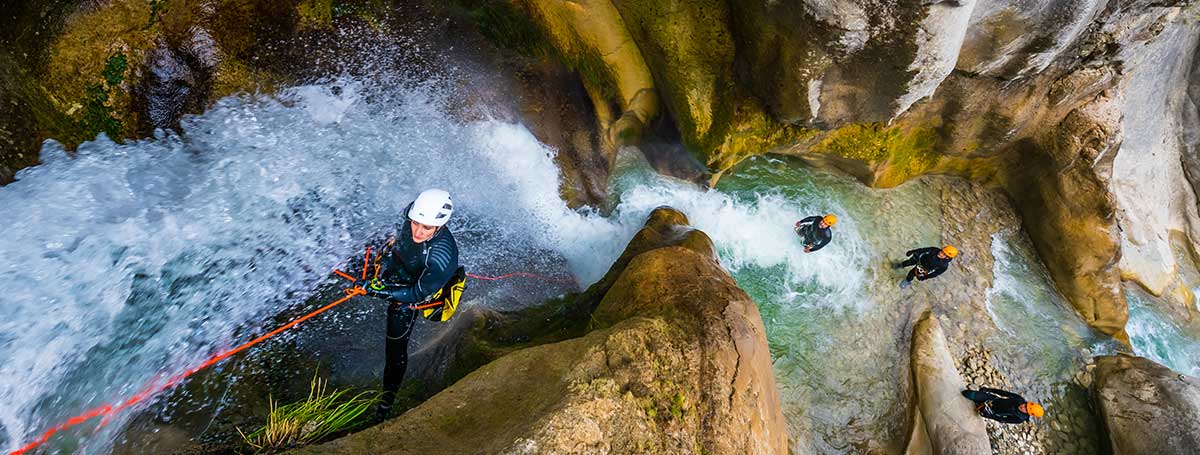 Referencia de barranquismo: descenso con cuerda junto a una cascada en un cañón con agua.