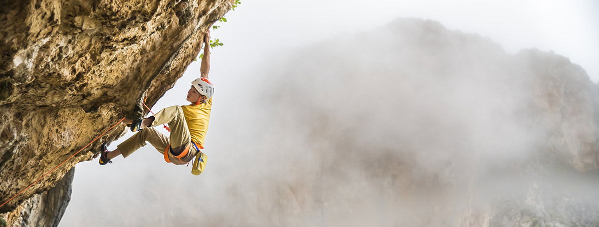 Referencia de escalada en roca: escalador asegurado con cuerda supera una pared natural desplomada.