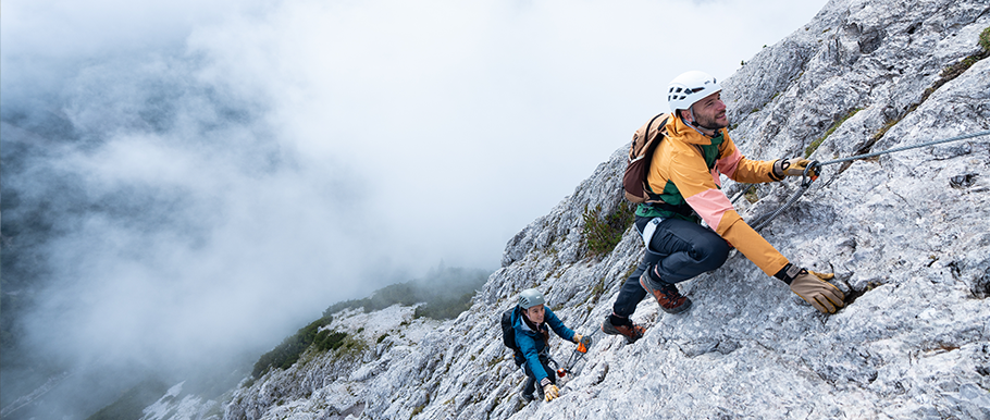 Referencia de vía ferrata: dos personas equipadas progresan por una pared rocosa con cable fijo.